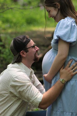 A loving couple share a tender moment outdoors as they anticipate their new arrival wearing a blue dress.