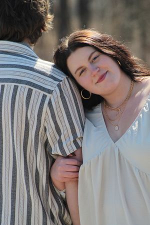A couple shares an intimate moment outdoors, with one person wearing a striped shirt and the other in white with layered necklaces.