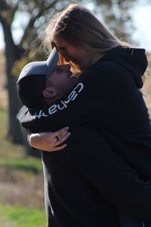 A couple sharing an intimate embrace outdoors wearing black hooded sweatshirts on a sunny autumn day.