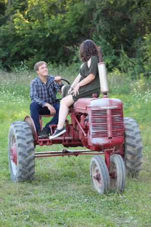 Couple posing on a vintage red tractor in a summer meadow.