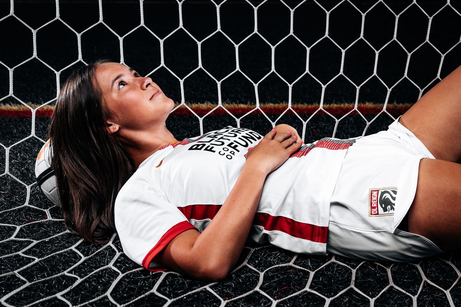 A soccer player from Reign Academy lays down on a soccer net while resting her head on a ball.