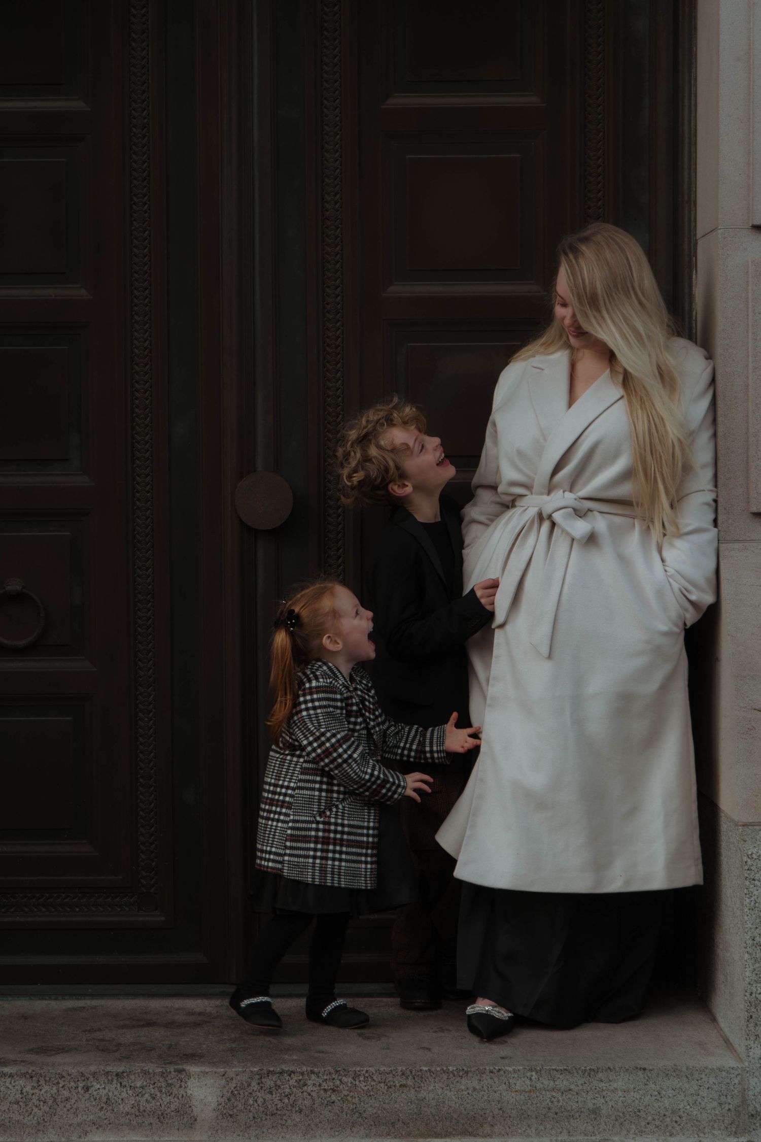 Two figures in winter coats sharing a tender moment outside a dark doorway.