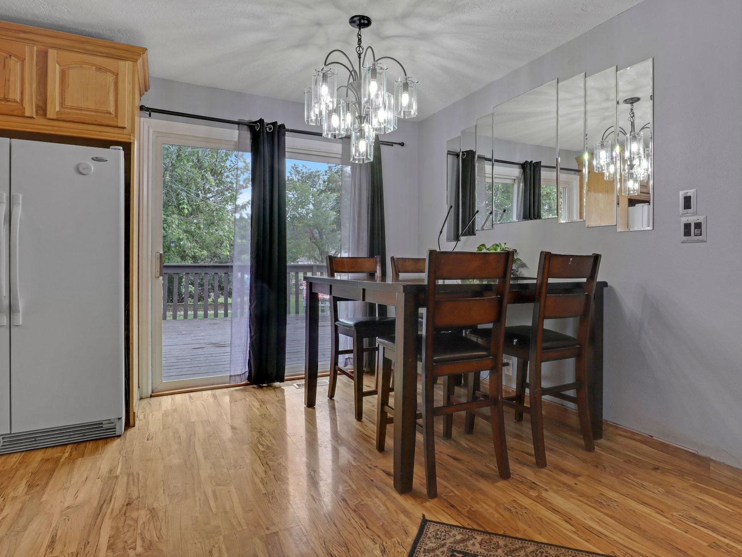 Bright dining area with hardwood floors, chandelier, bar-height table, and sliding glass door to outdoor deck.