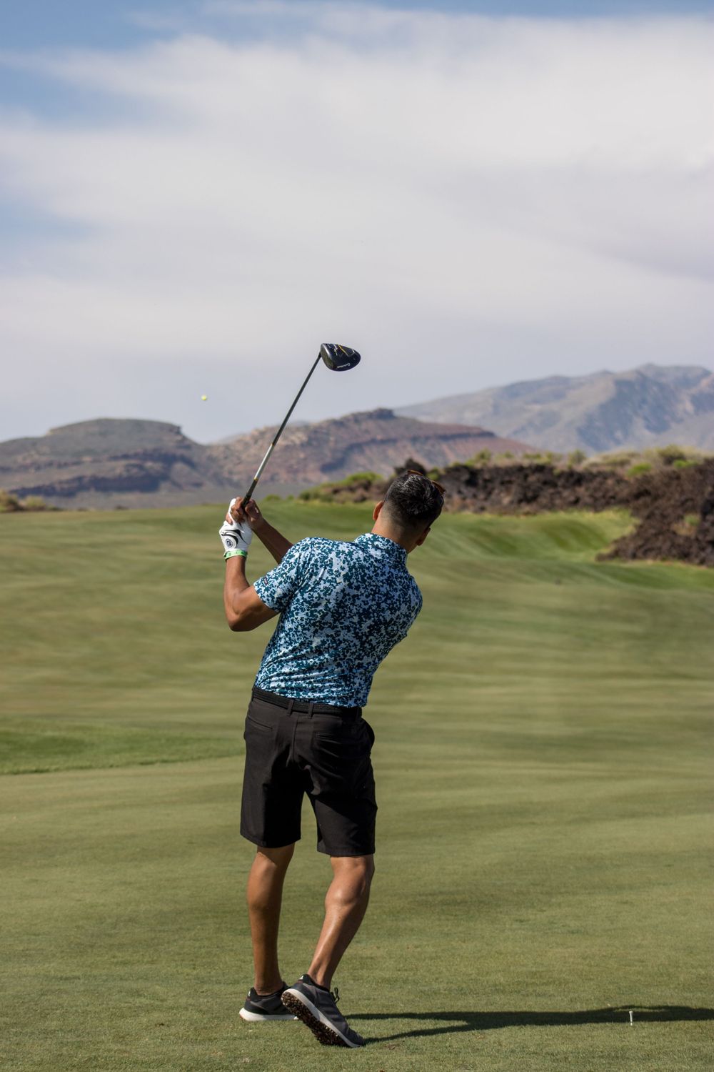 Male golfer completes powerful driver swing on scenic desert golf course with mountain views.