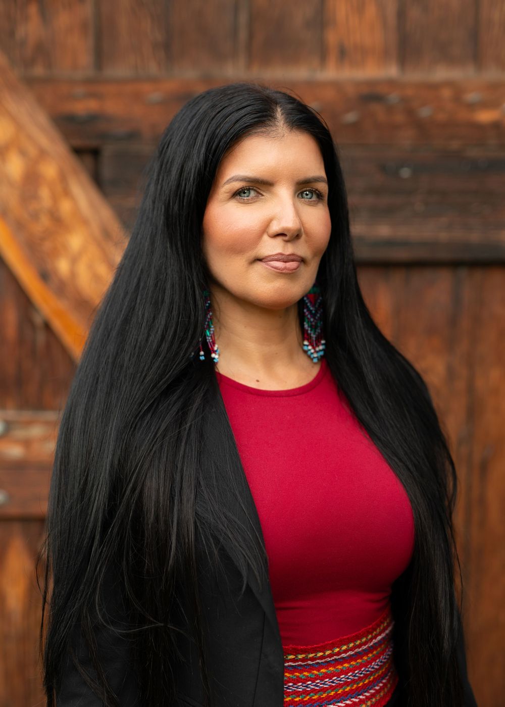 Woman in red shirt and black blazer smiling at camera with blurred wooden background - Okanagan headshot by Tania Veitch.