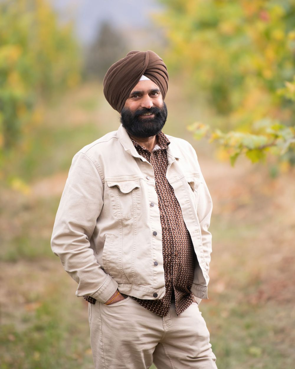Winemaker and owner of Little Straw Winery wearing brown turban and cream jacket standing in vineyard - Okanagan portrait by Tania Veitch.