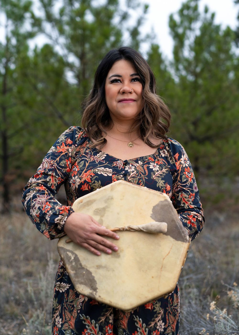 Woman holding hide-covered drum and drumstick, looking into the distance - Okanagan portrait by Tania Veitch.