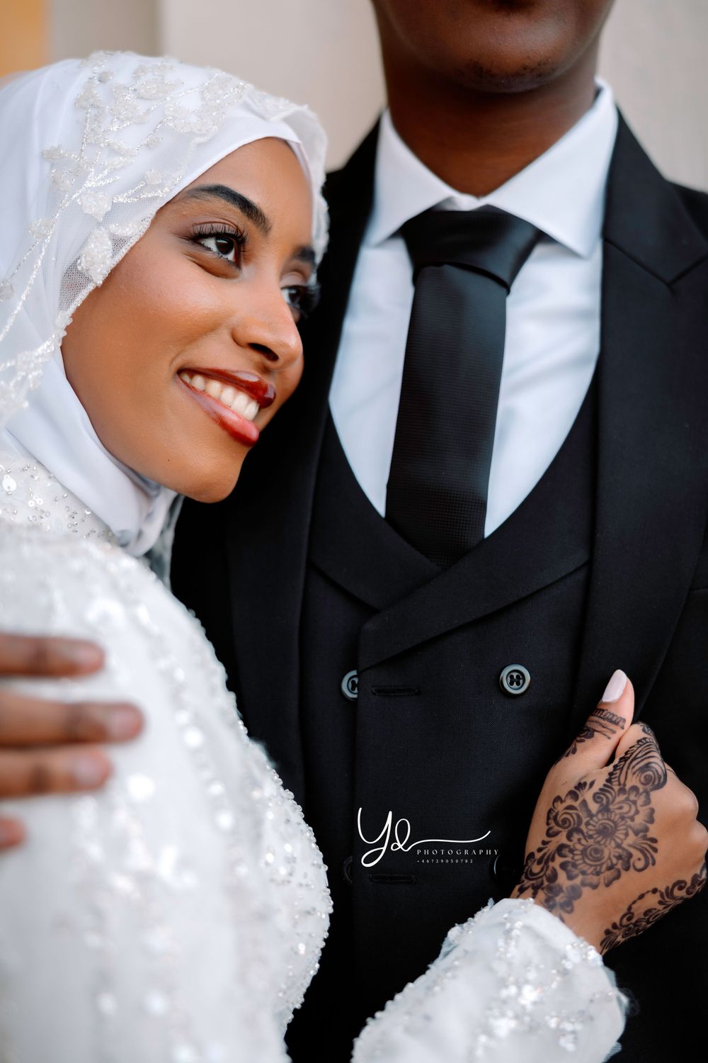 Elegant bride in white hijab and lace dress with intricate henna designs.