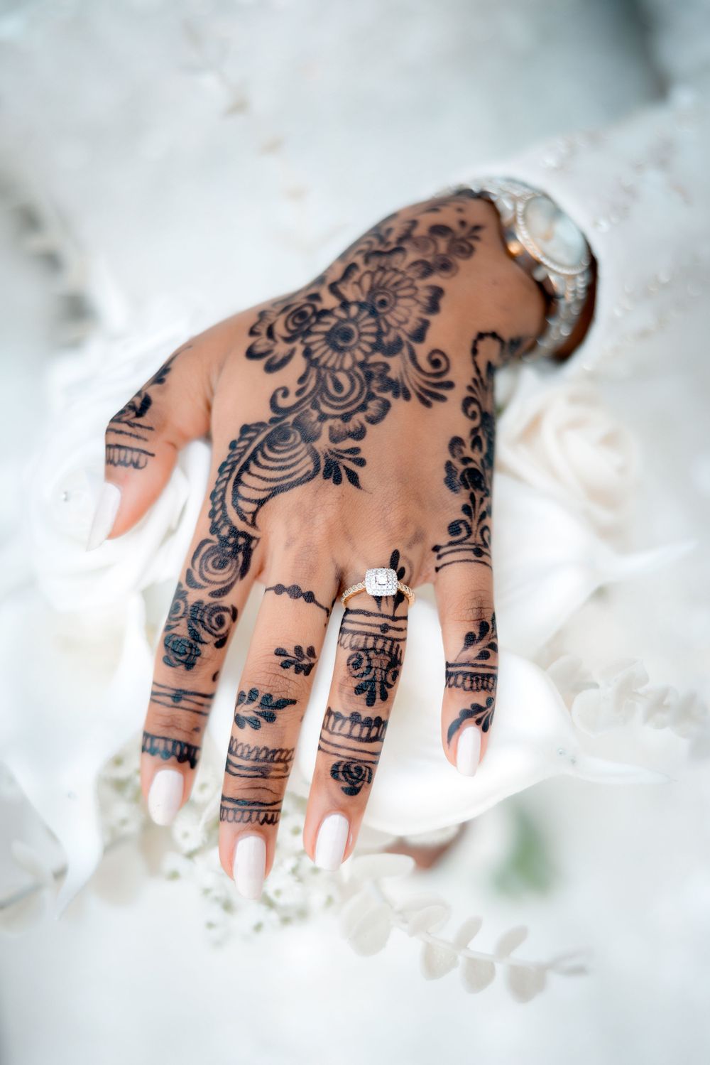 Close-up of beautiful henna design on bride's hand against white lace fabric.