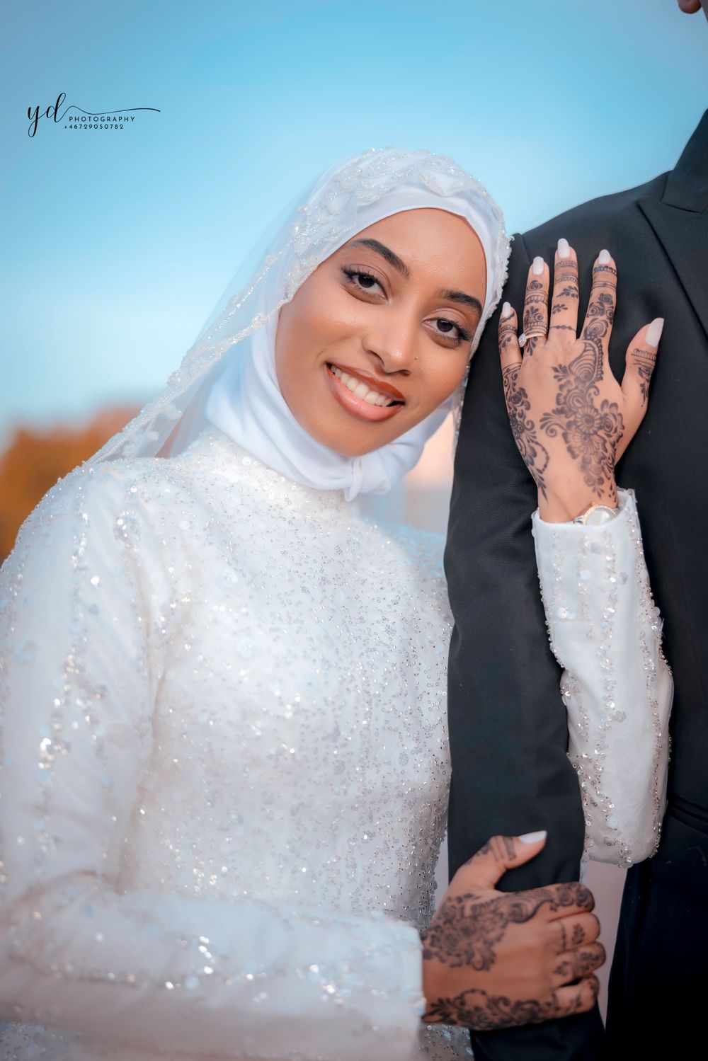 A bride wearing a white sequined hijab and dress shows off intricate henna designs on her hands.