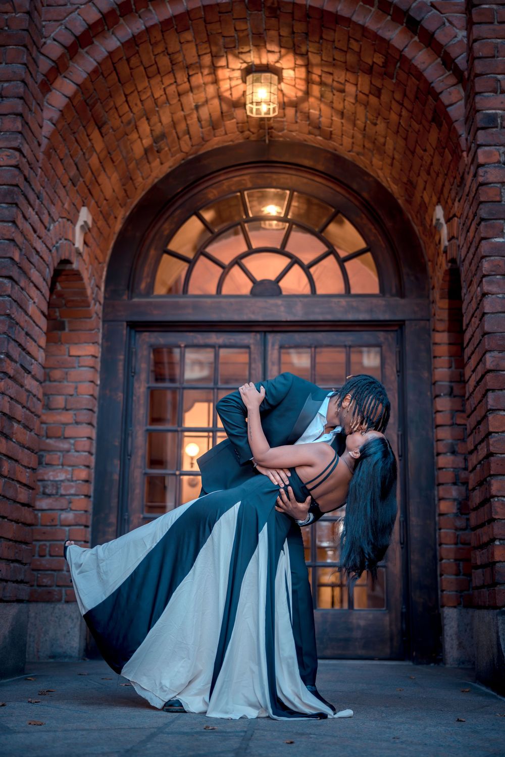 Dramatic dip pose of couple in formal wear beneath illuminated brick archway.
