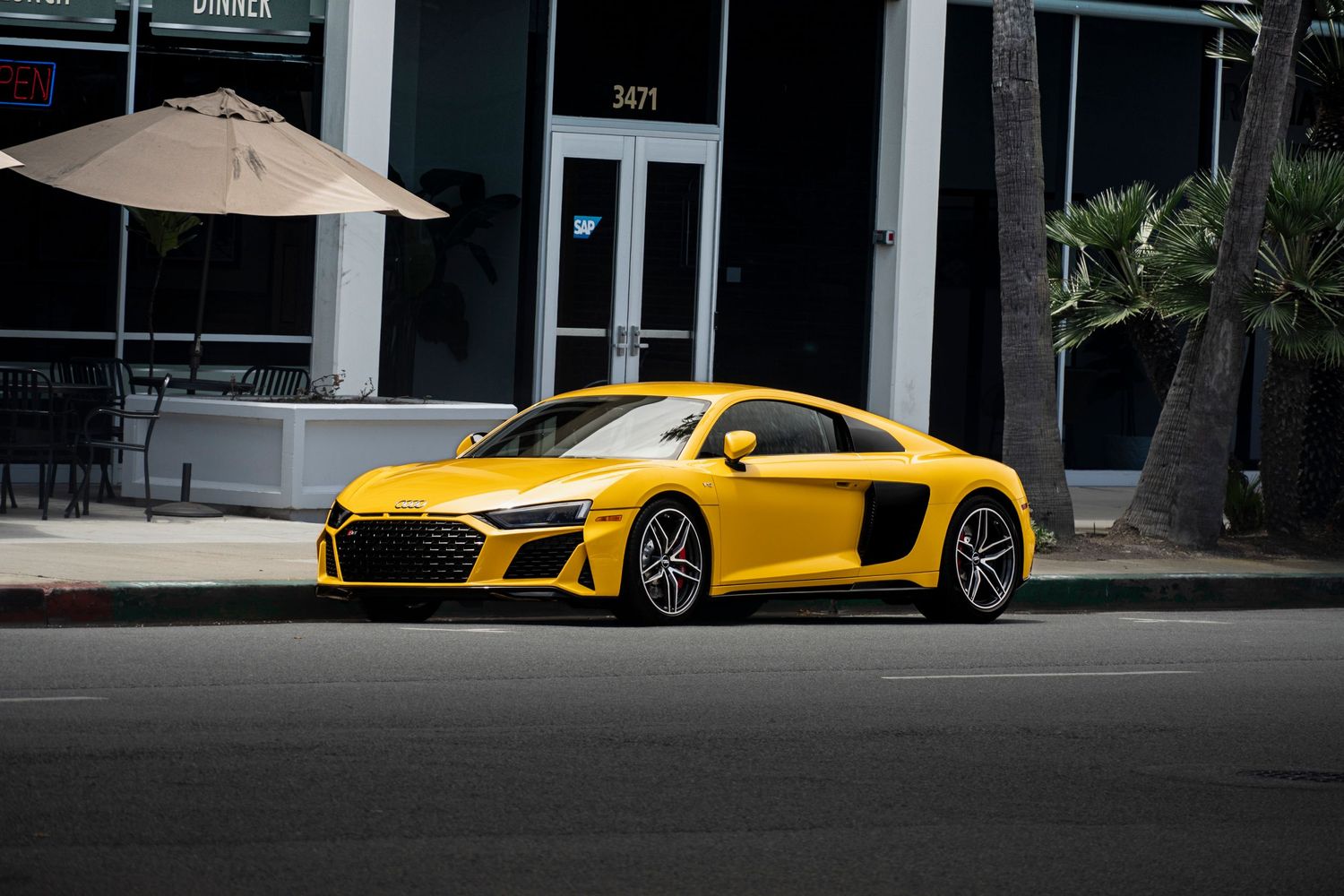 Yellow Audi R8 V10 supercar parked on a street in front of a modern building.