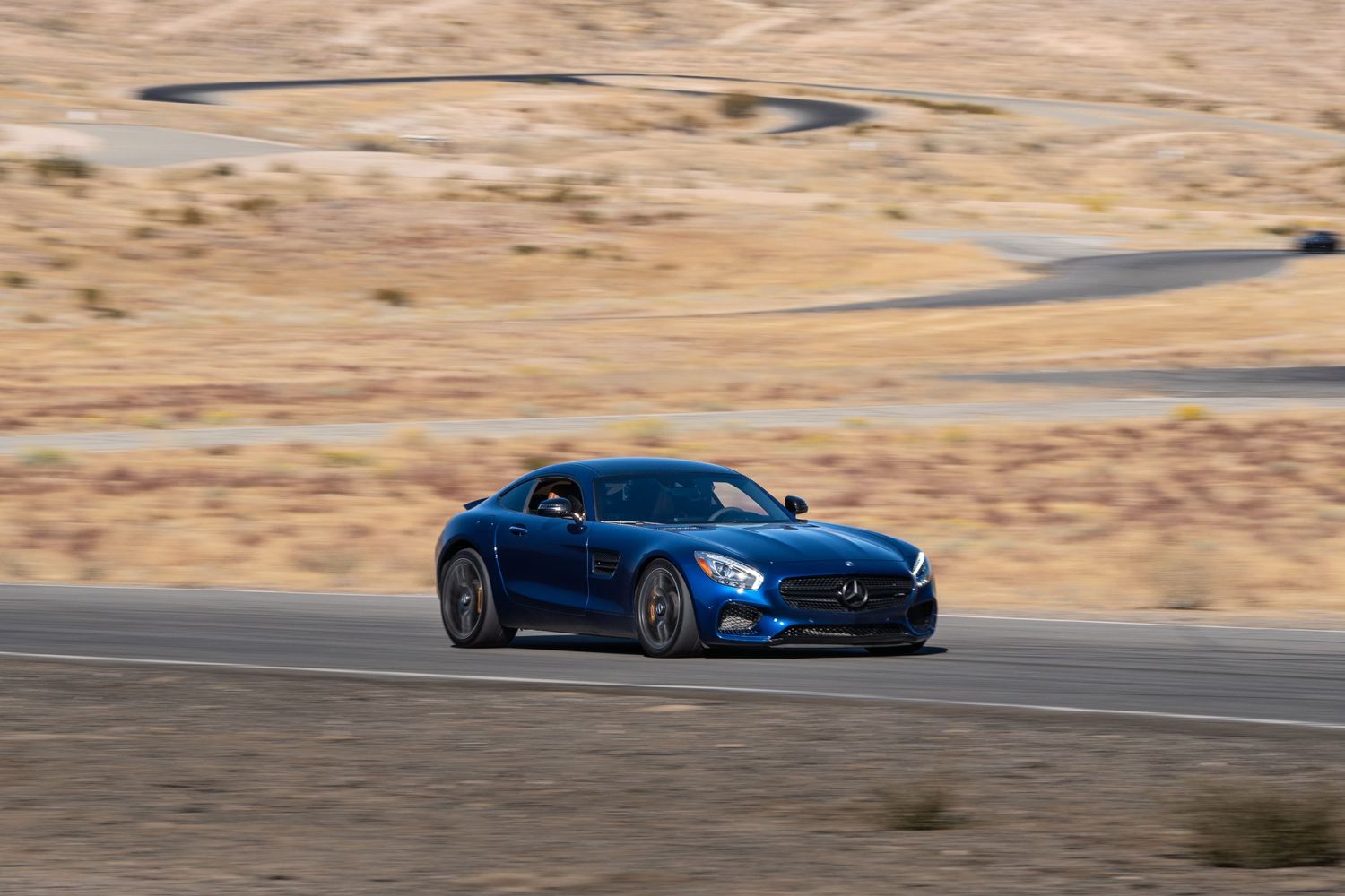 Blue Mercedes-AMG GT S coupe cornering on a desert race track.