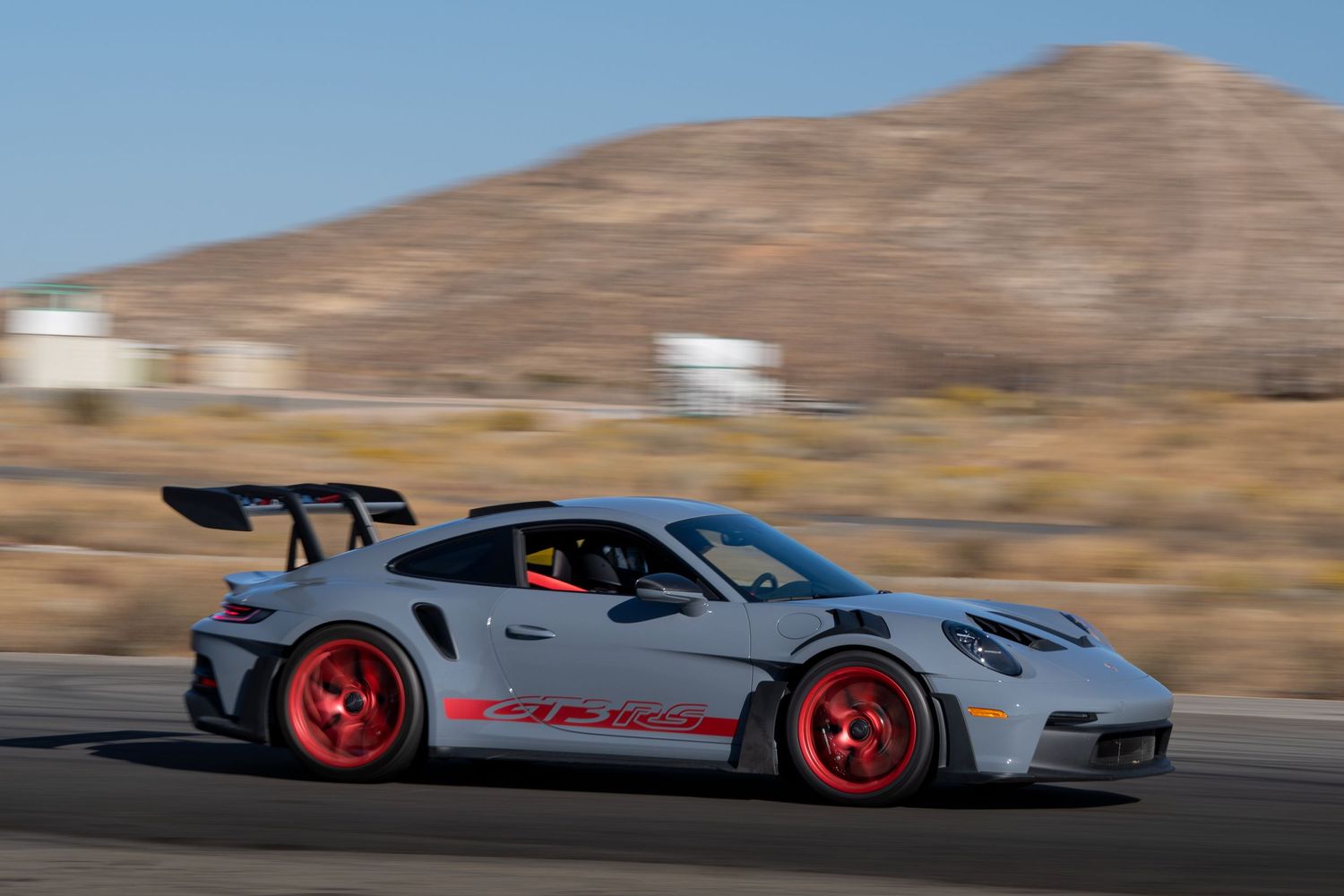 Grey Porsche 911 GT3 RS with red wheels racing on a desert track.