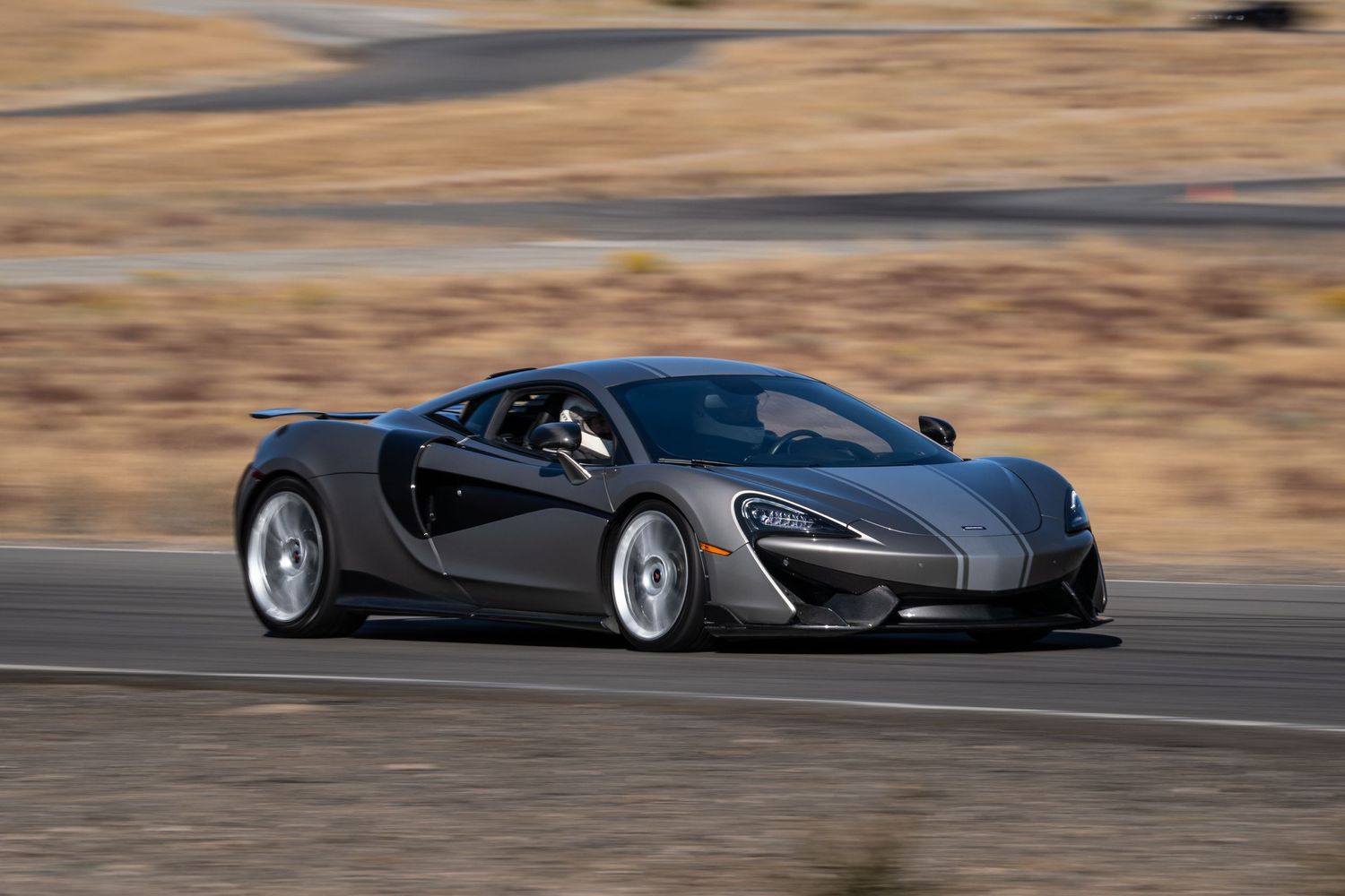 Gray McLaren 570S supercar driving fast on a desert race track.