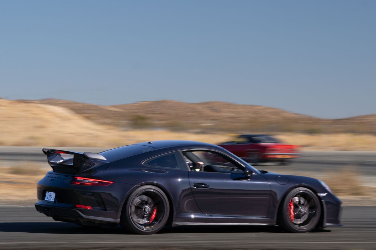 Dark blue Porsche 911 GT3 speeding on a race track in the desert.