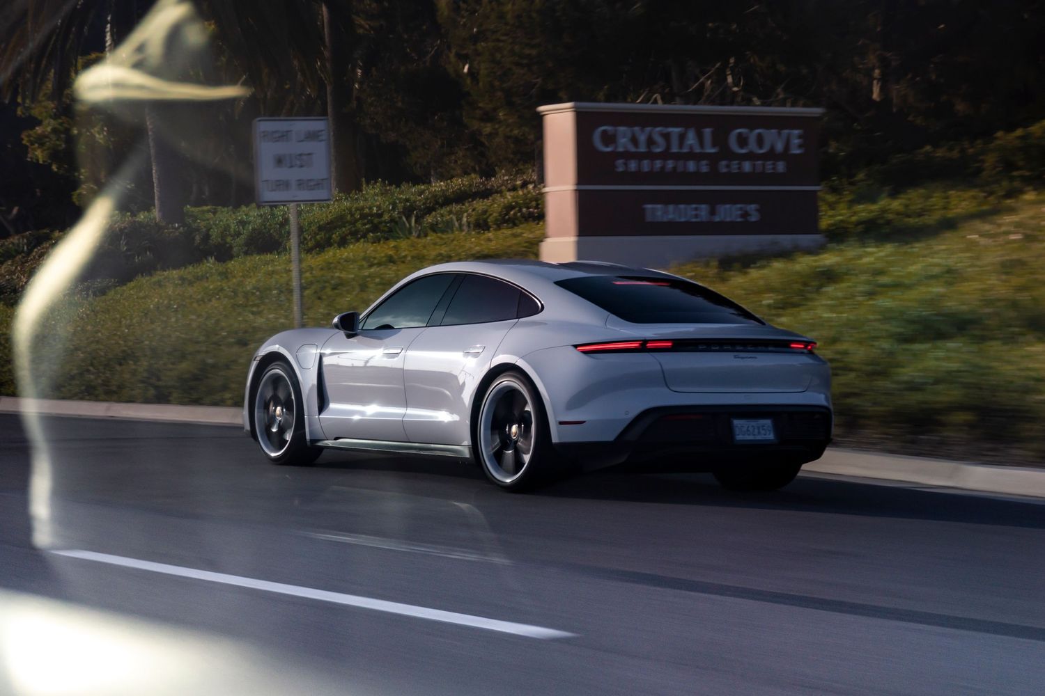 Silver Porsche Taycan driving past Crystal Cove Shopping Center in California.