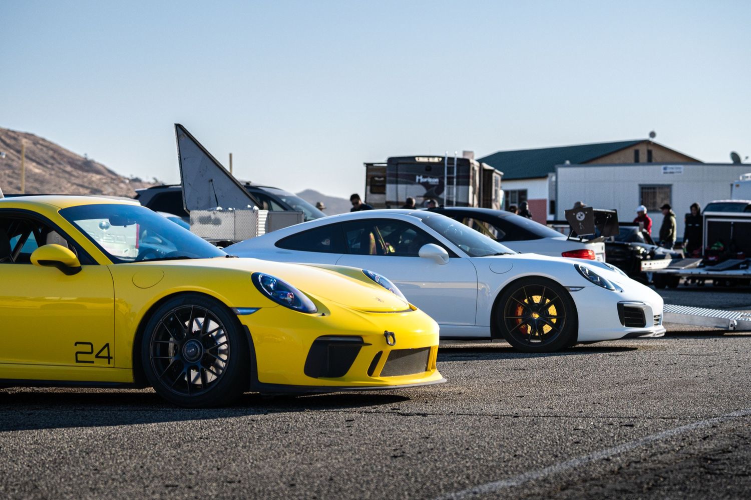 Yellow and white Porsche 911 GT3 race cars lined up on track.