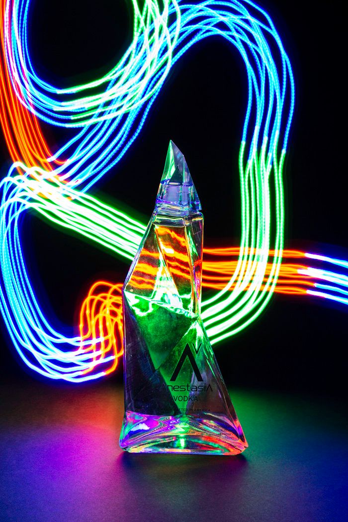 Colorful light trails swirl around a triangular glass bottle in dark setting.