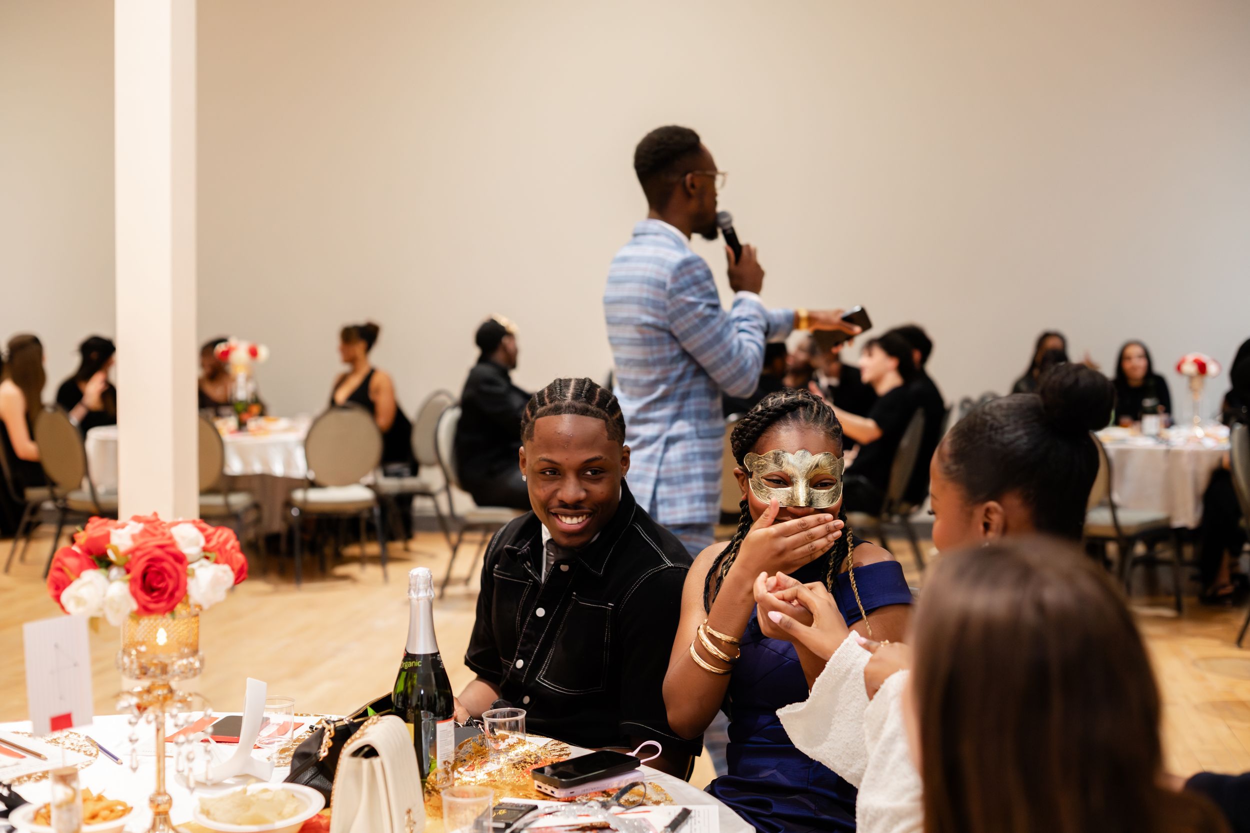 People seated at tables during a social gathering or event in a bright indoor venue.