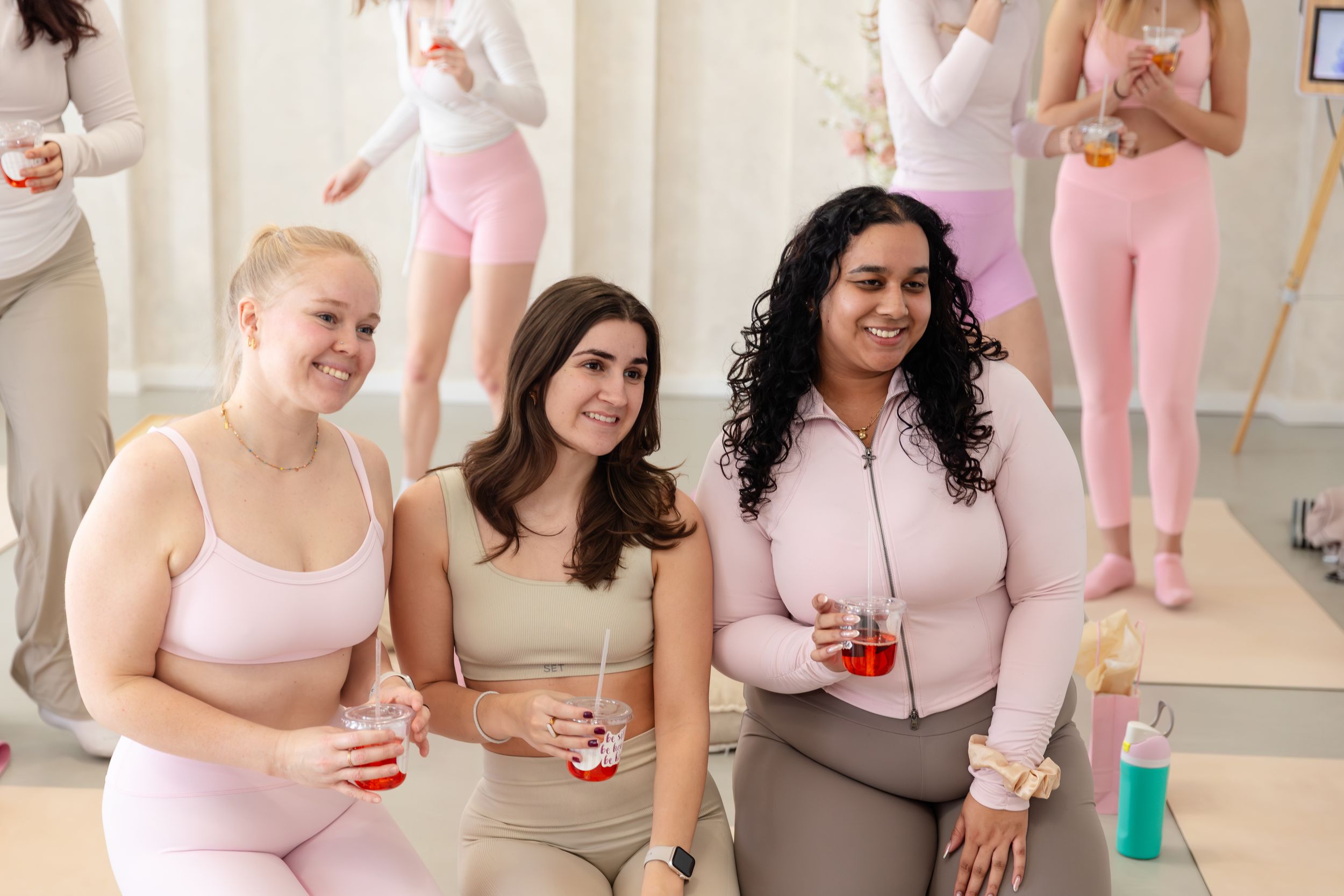 A group wearing pink outfits poses together at a ballet studio with ballet barres and mirrors visible.