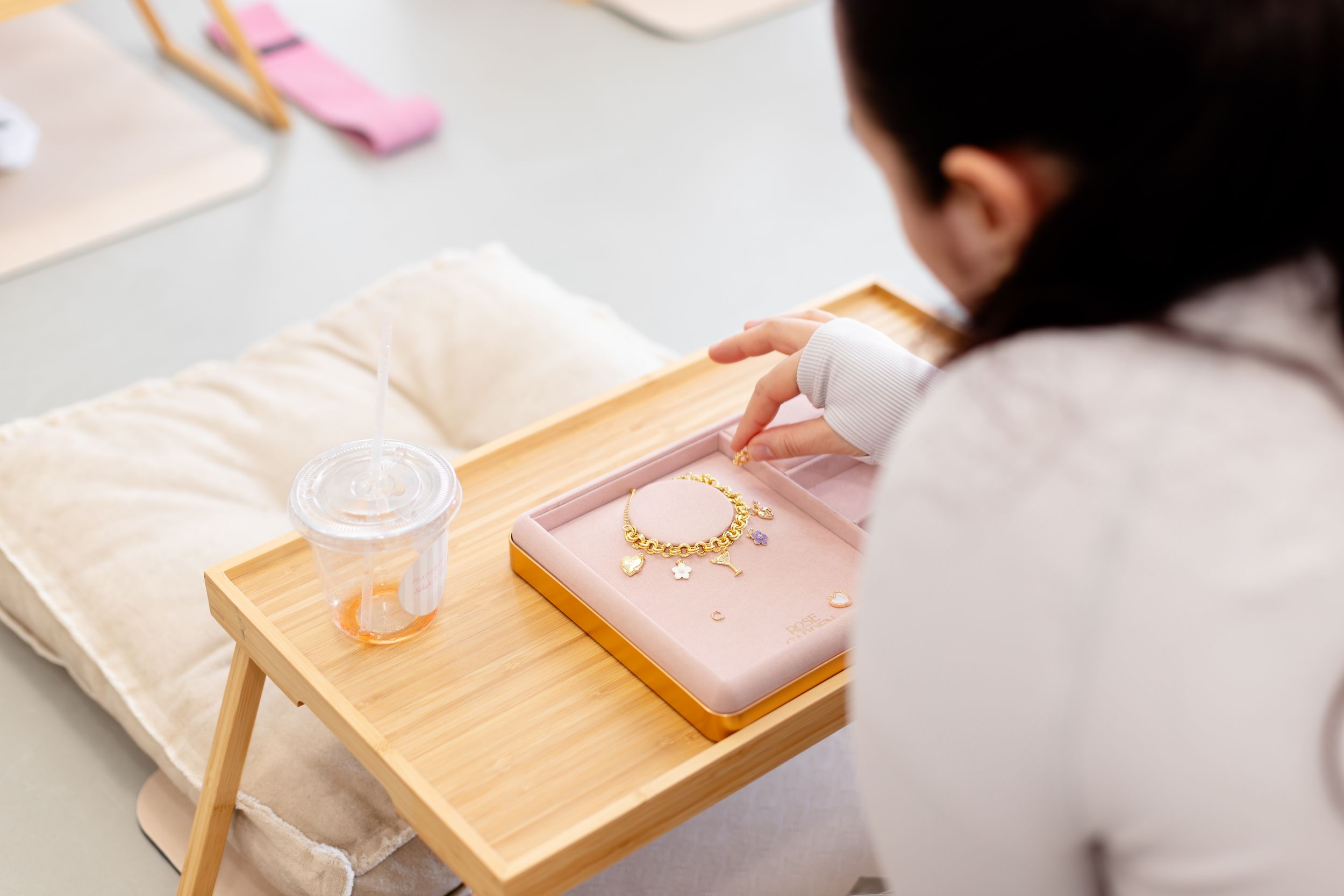 Elegant pink and gold jewelry display setup with wooden trays and soft fabric backdrops.