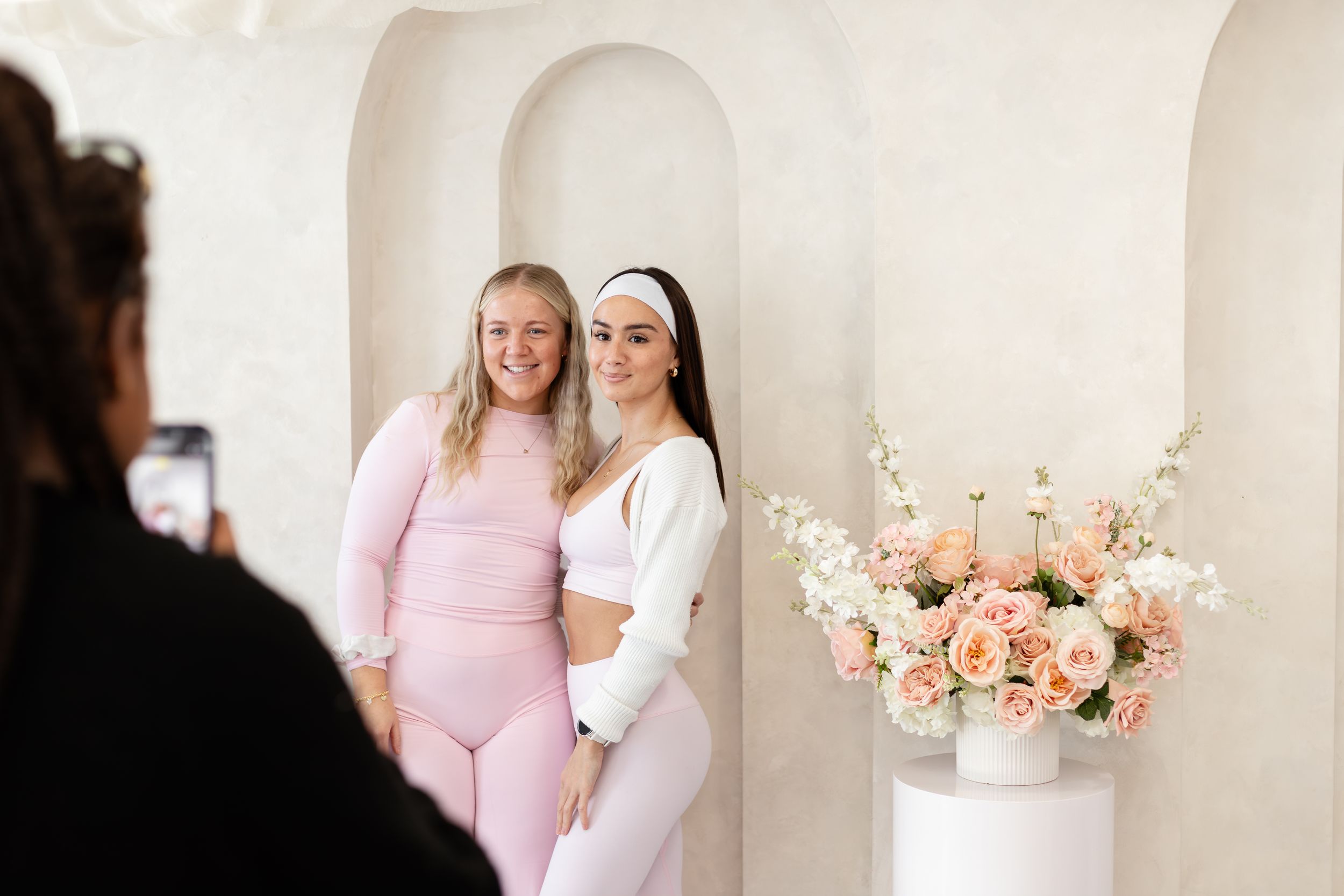 Two people in pink and white outfits share a joyful moment together in a bright indoor setting.