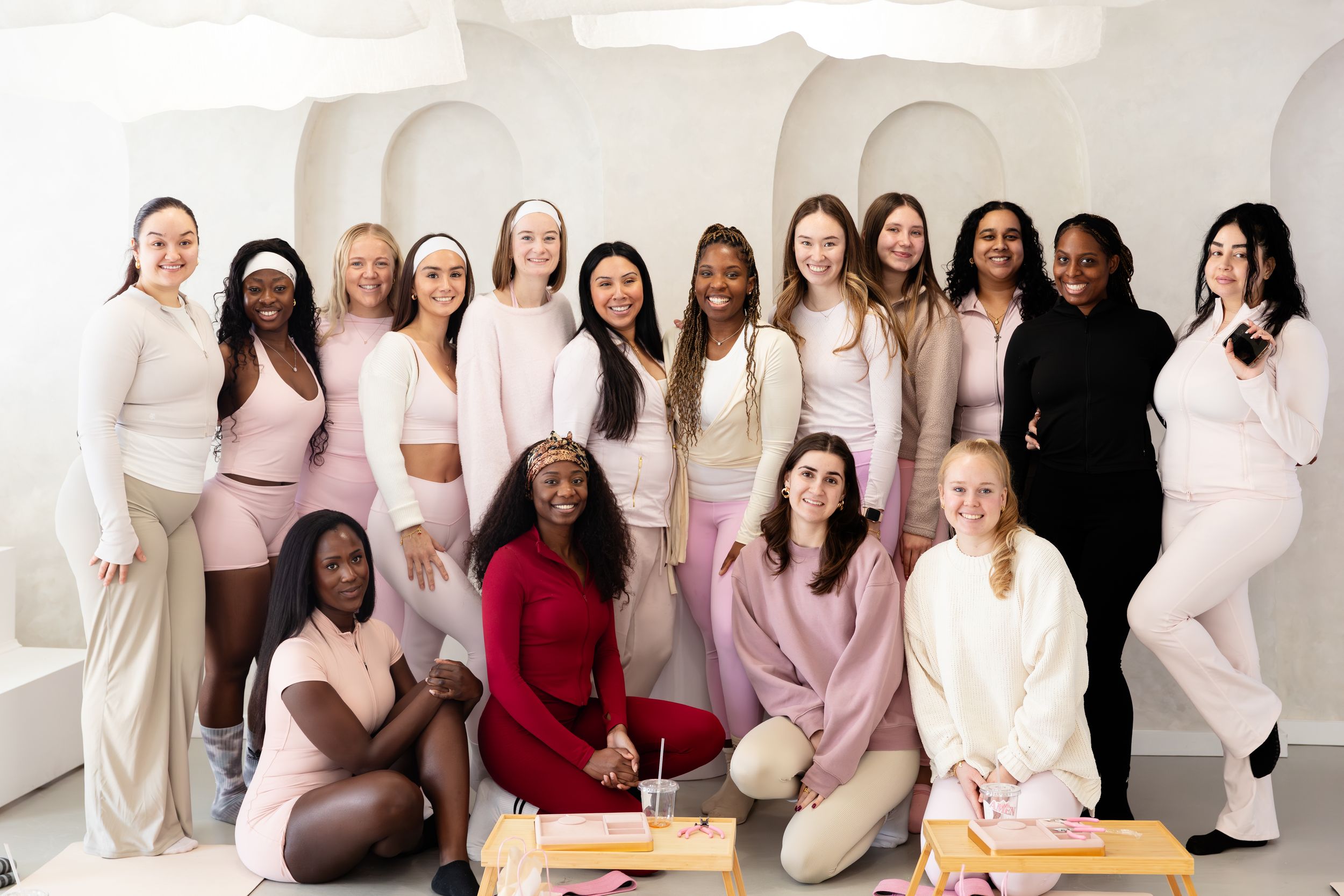 A group of women wearing cozy loungewear and robes pose together for a lifestyle photoshoot in a bright studio setting.