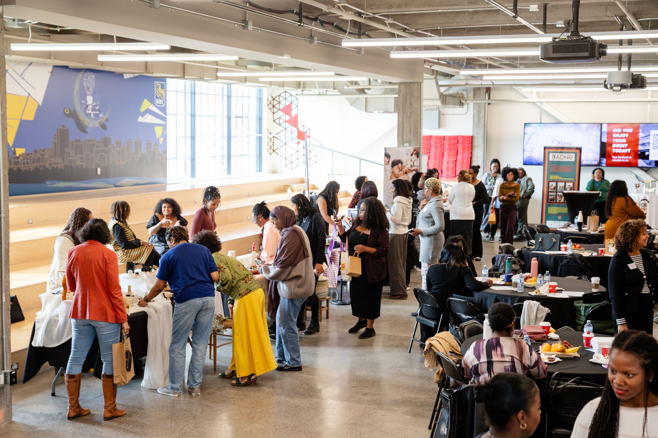 People stand in line at a busy indoor event space with white walls and industrial ceiling.