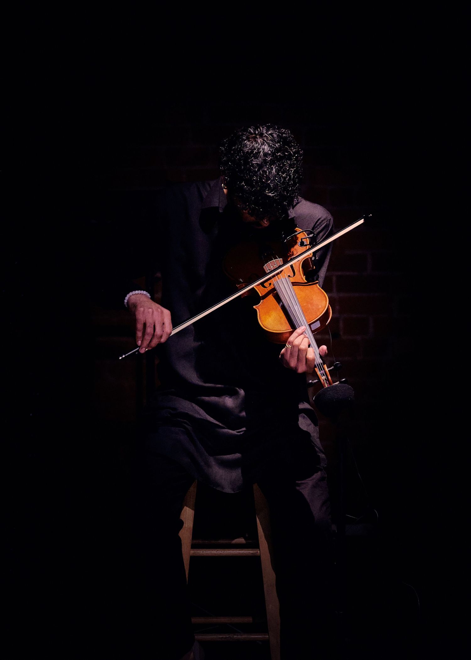 Dramatic low-light portrait of violinist performing in dark setting.