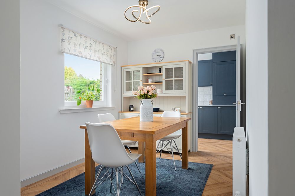 Modern dining area with white walls, hardwood floors, and natural light streaming through windows.