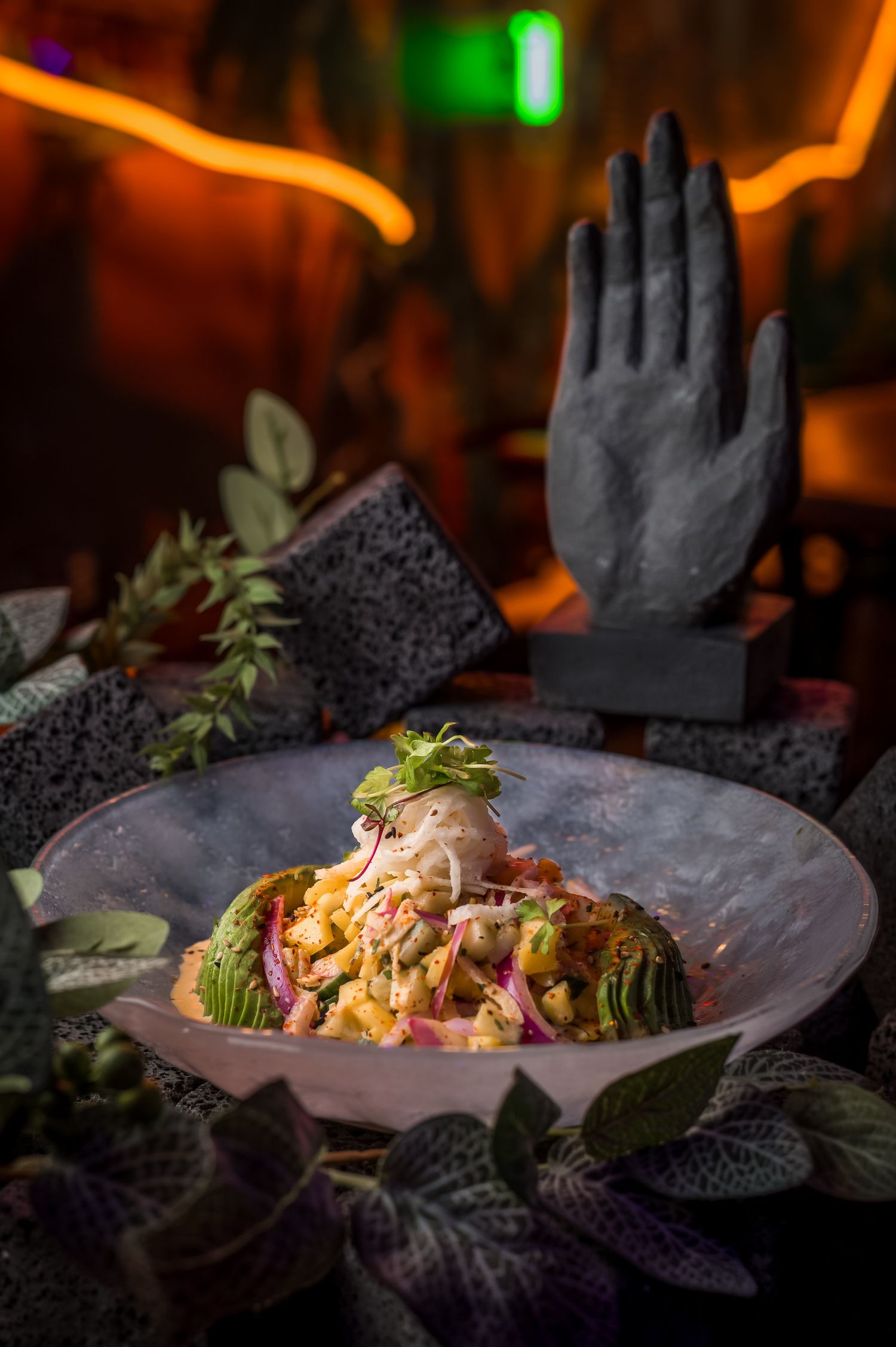 Artistic plating of seafood dishes on dark plates with dramatic lighting and hand sculptures.