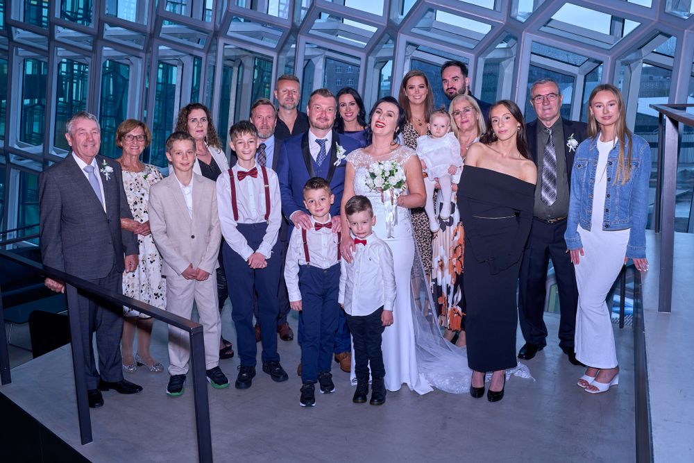 Wedding party group poses together inside modern glass-walled venue with blue-tinted architectural details.