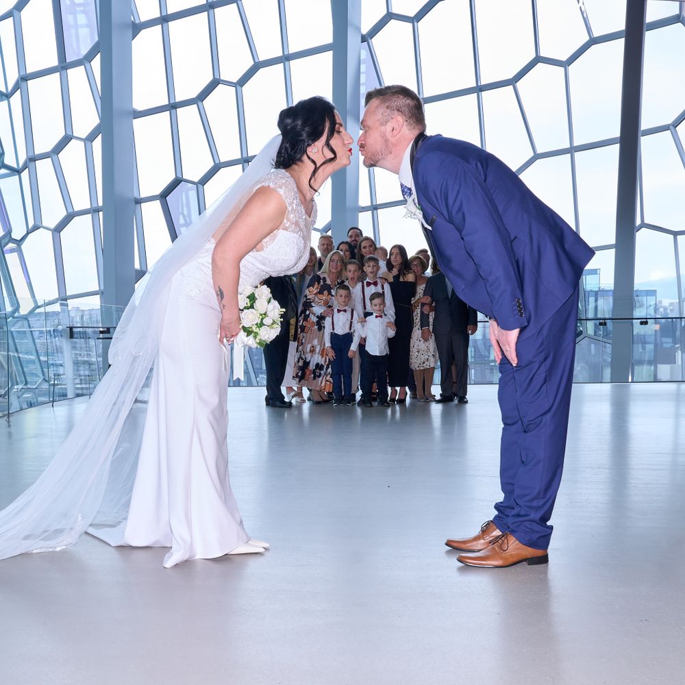 A bride and groom share a romantic moment in front of their wedding guests at a modern venue with large windows.