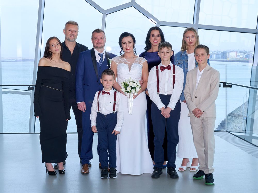 Wedding party poses together in modern venue with floor-to-ceiling windows overlooking waterfront.