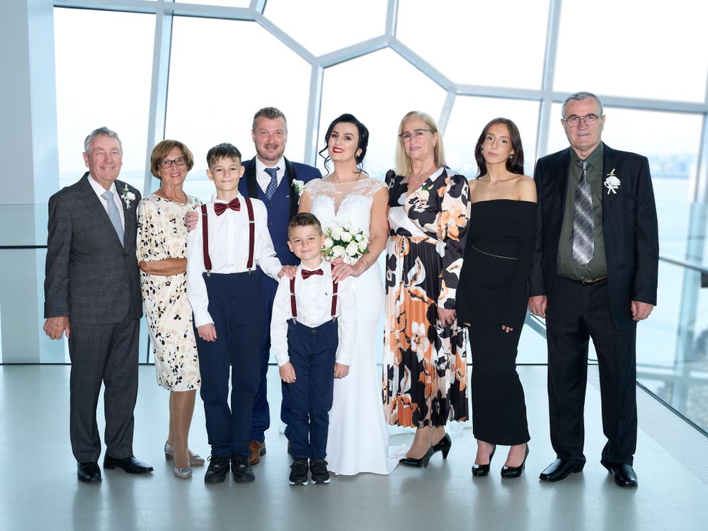 A group in formal attire poses together in a modern building with floor-to-ceiling windows and natural light.