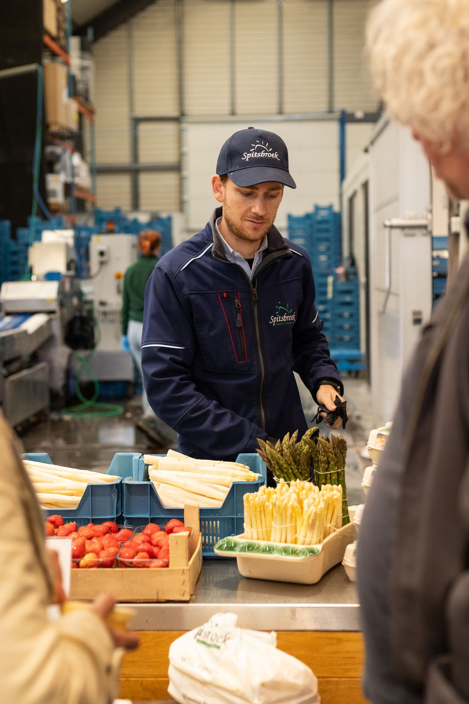 Staff member in blue uniform organizing fresh vegetables and ingredients at a wooden prep station.