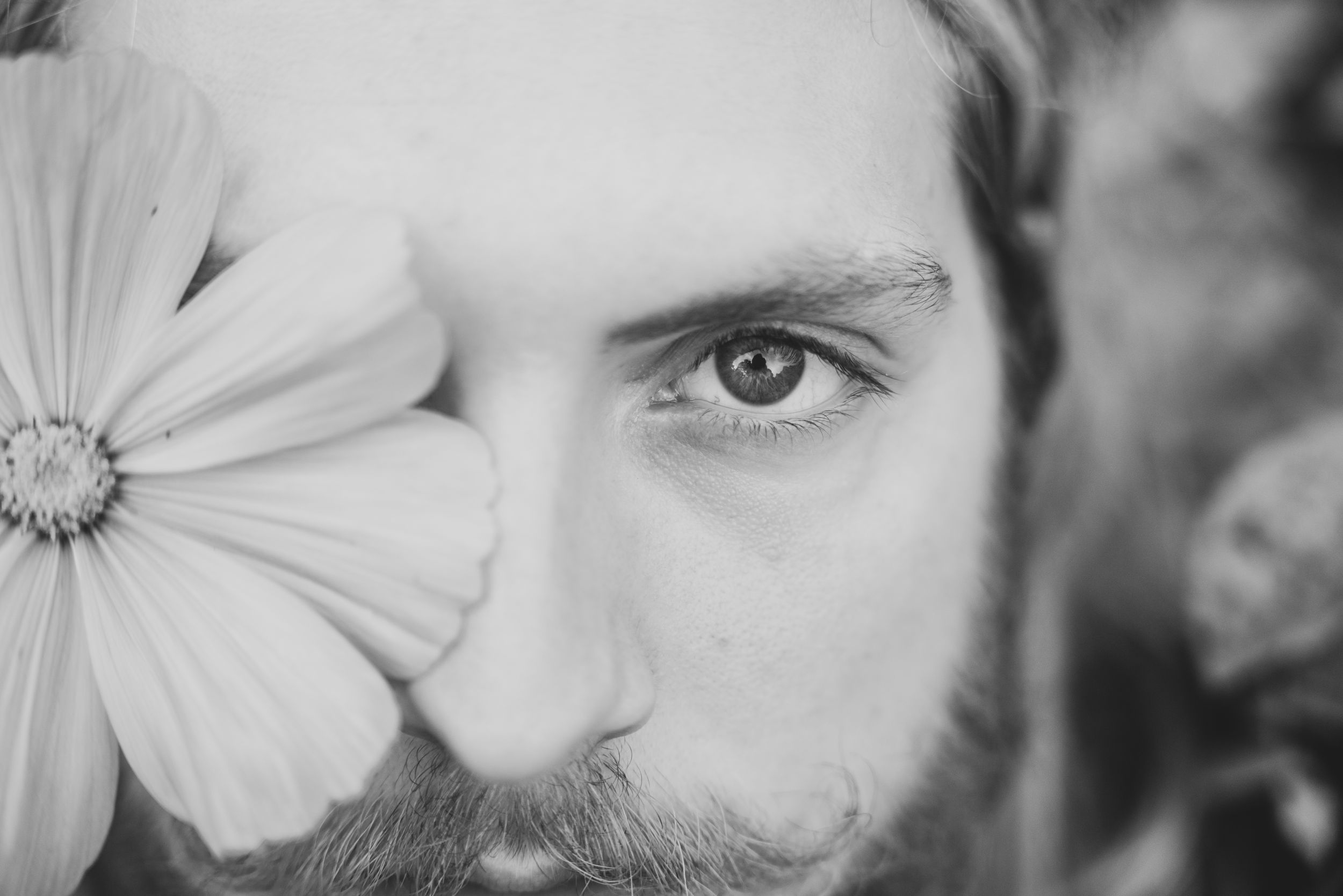A artistic black and white portrait with a white flower partially covering the subject's face.