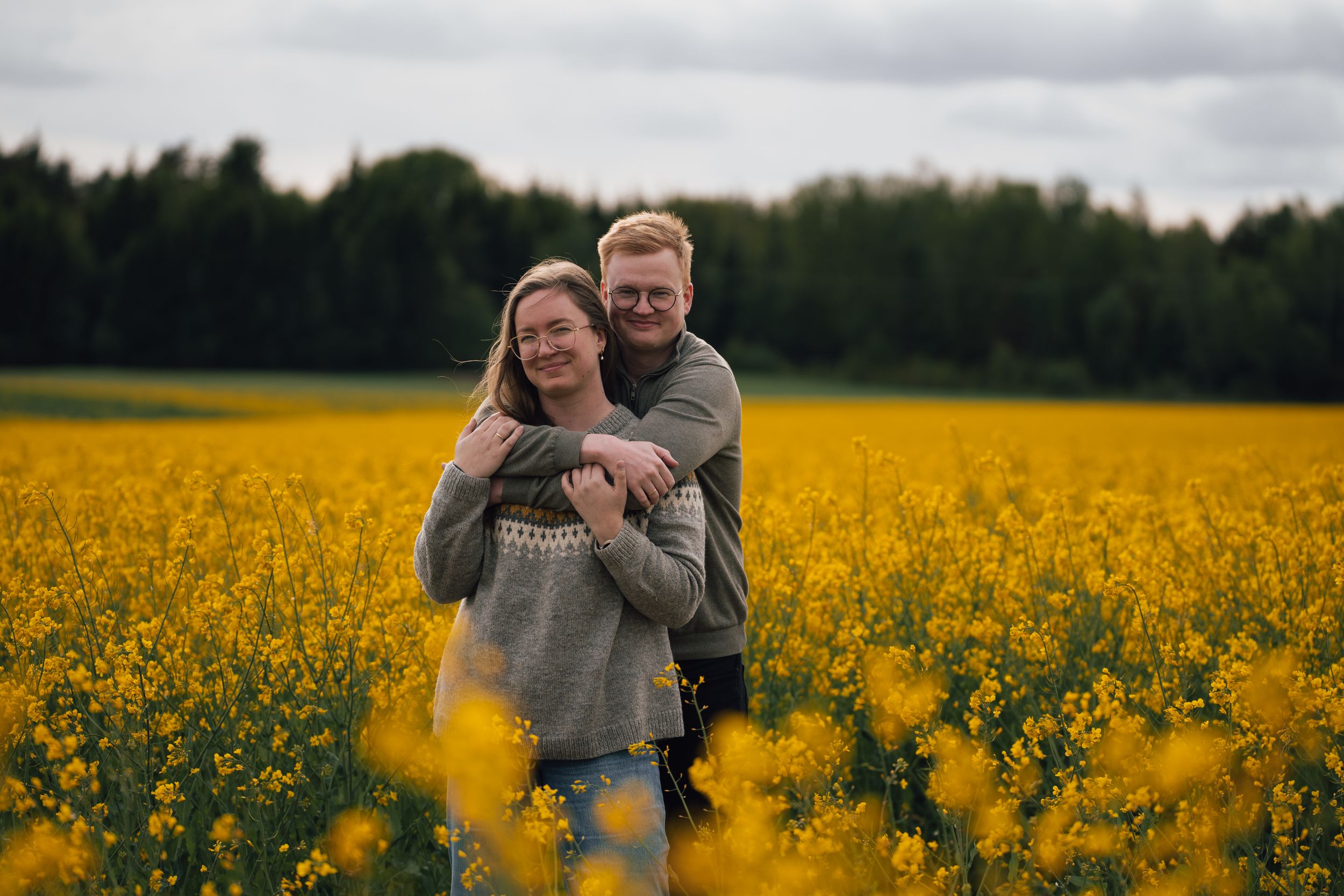 Couple embracing in a vibrant yellow canola flower field on an overcast day.