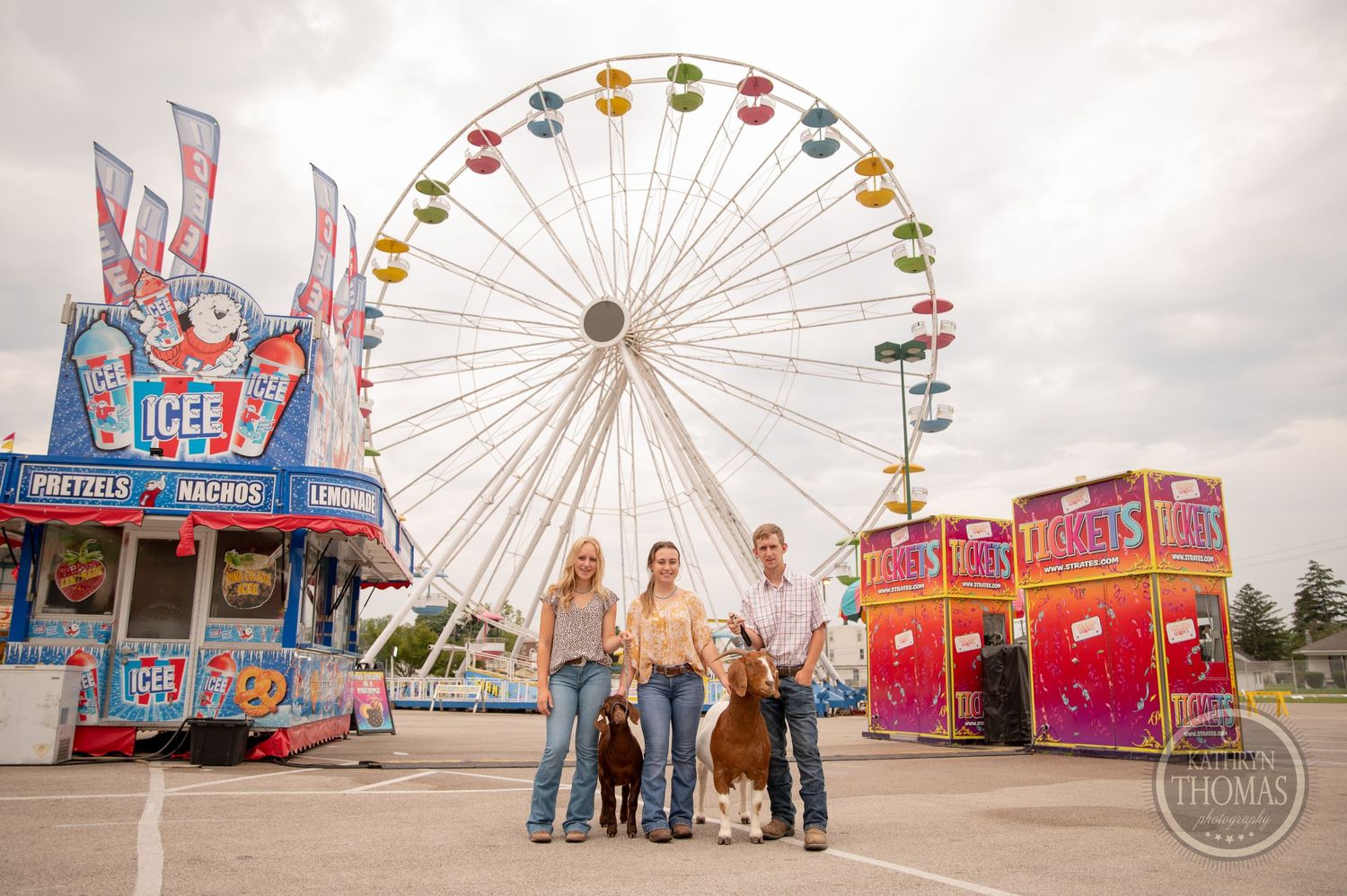 Family poses with their show cow in front of a Ferris wheel at a county fair.