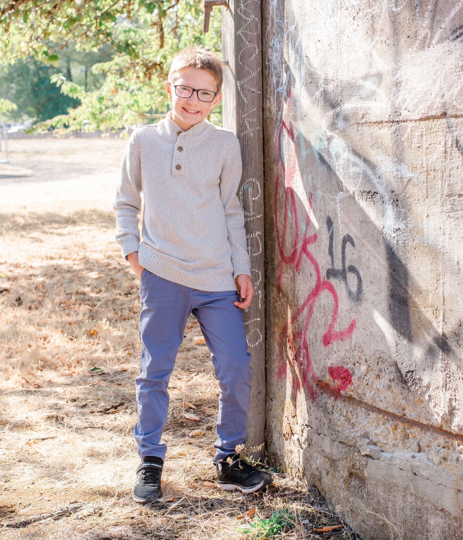 Child in casual wear posing against concrete wall with graffiti.