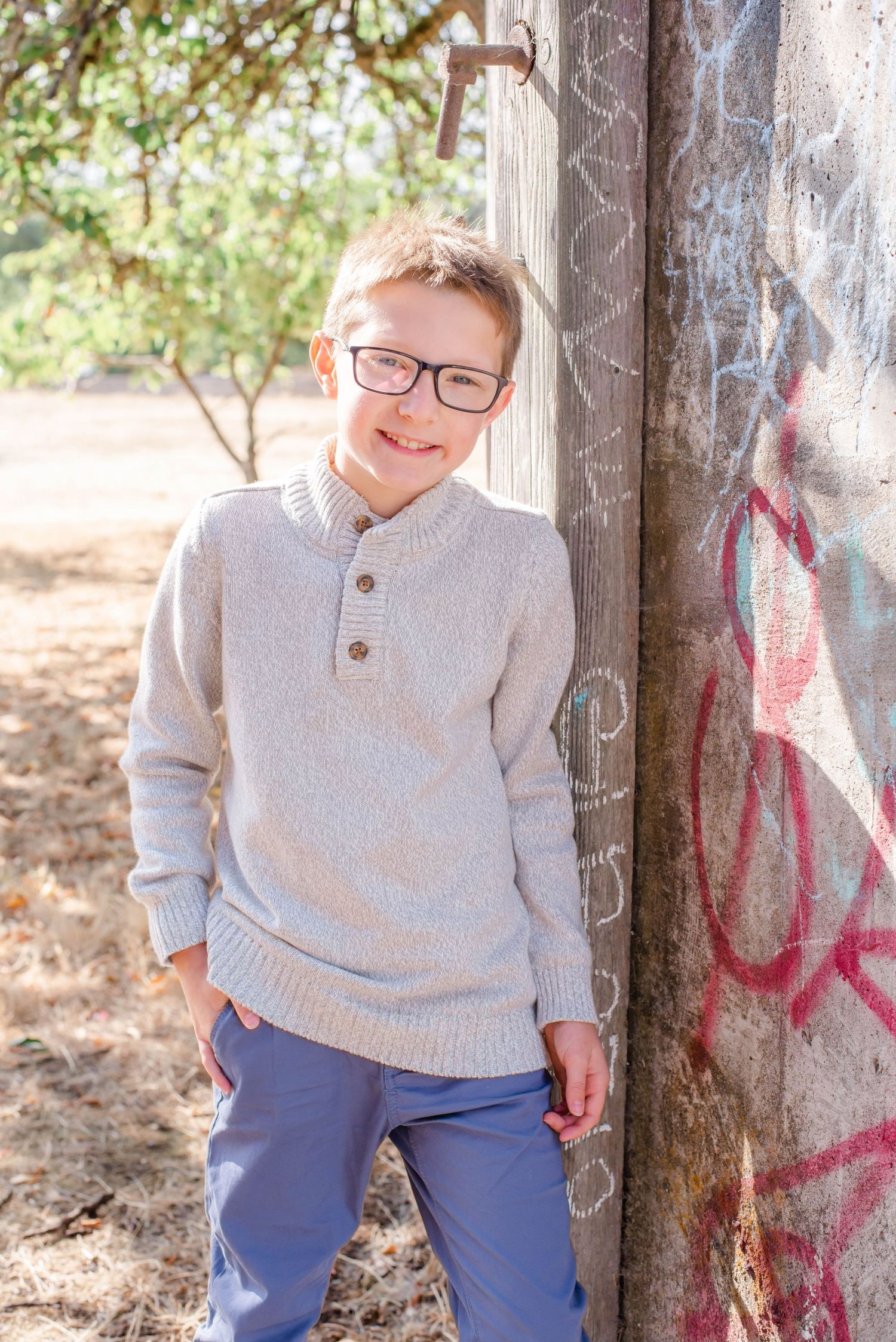 Child in cream sweater smiling and posing near concrete wall outdoors.