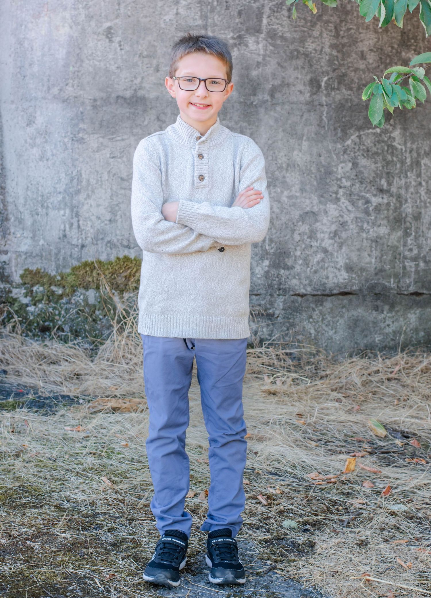 Young person in sweater and jeans standing confidently against outdoor wall.