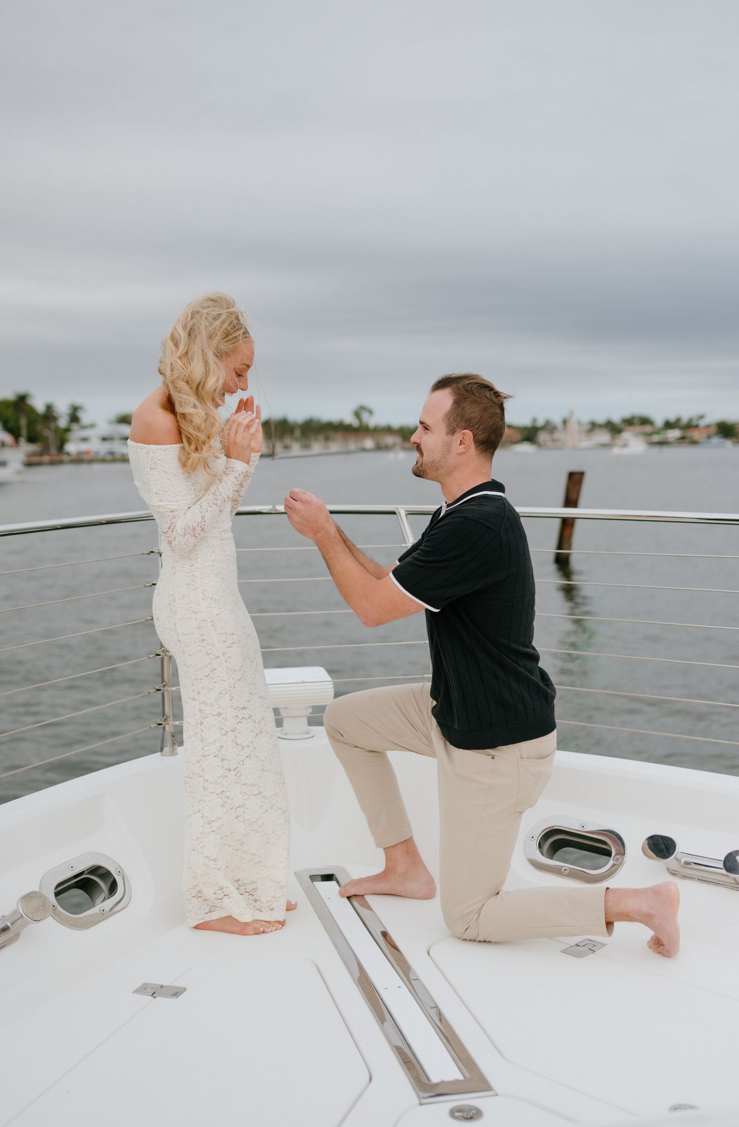 A romantic proposal moment on a boat deck with water and palm trees in the background.
