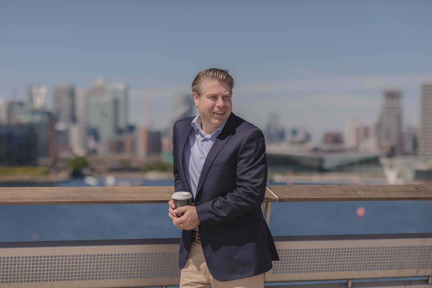 Person in business attire standing by railing with urban skyline in background.