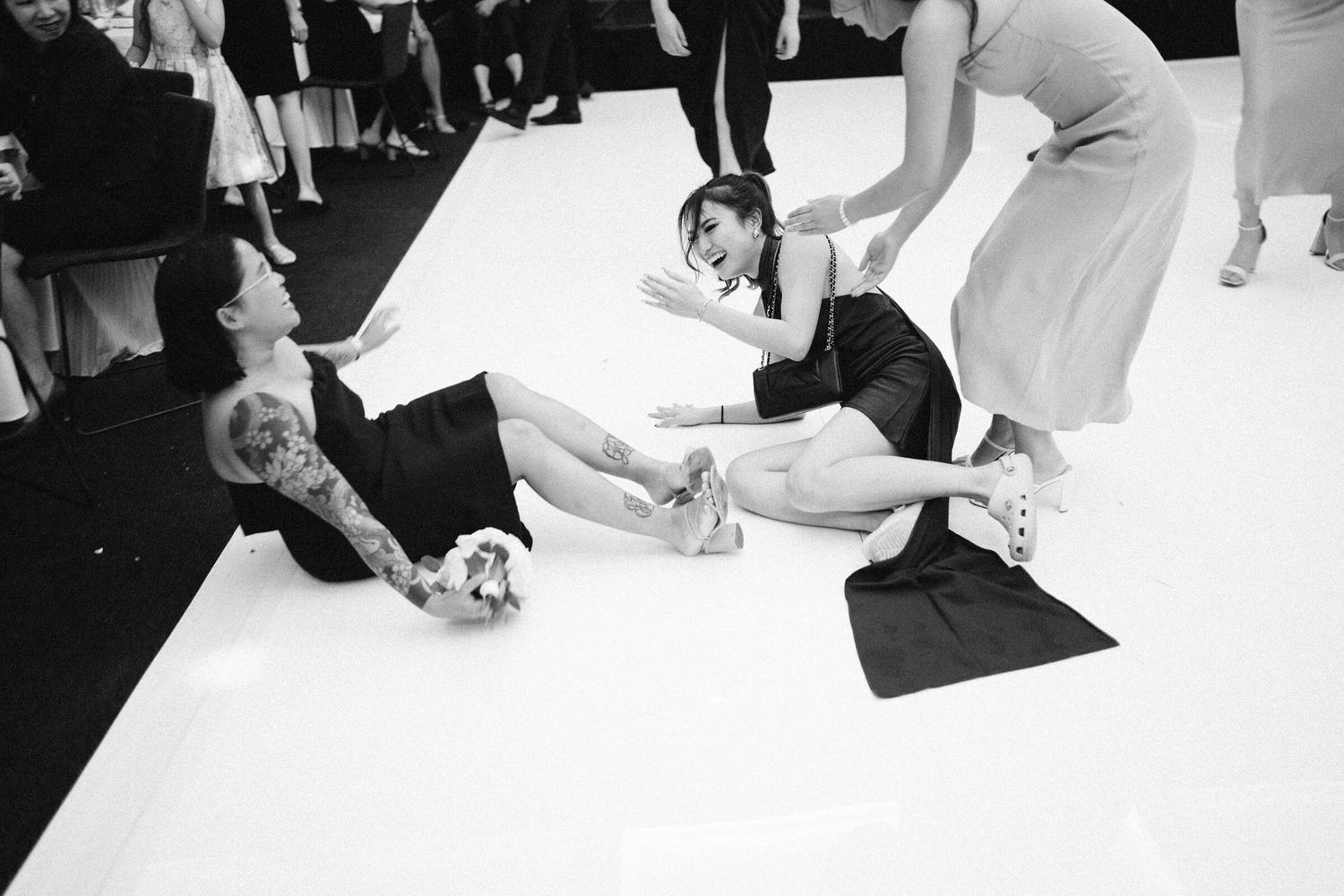 Girl laughing after falling during bouquet toss at wedding reception, Leonda by the Yarra, Melbourne. Fun, candid moment at the celebration.