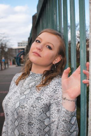 Portrait of someone in a gray snake print sweater posing against a green metal fence.