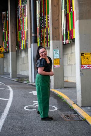 Casual portrait of someone in green pants and black top standing in an urban parking structure.