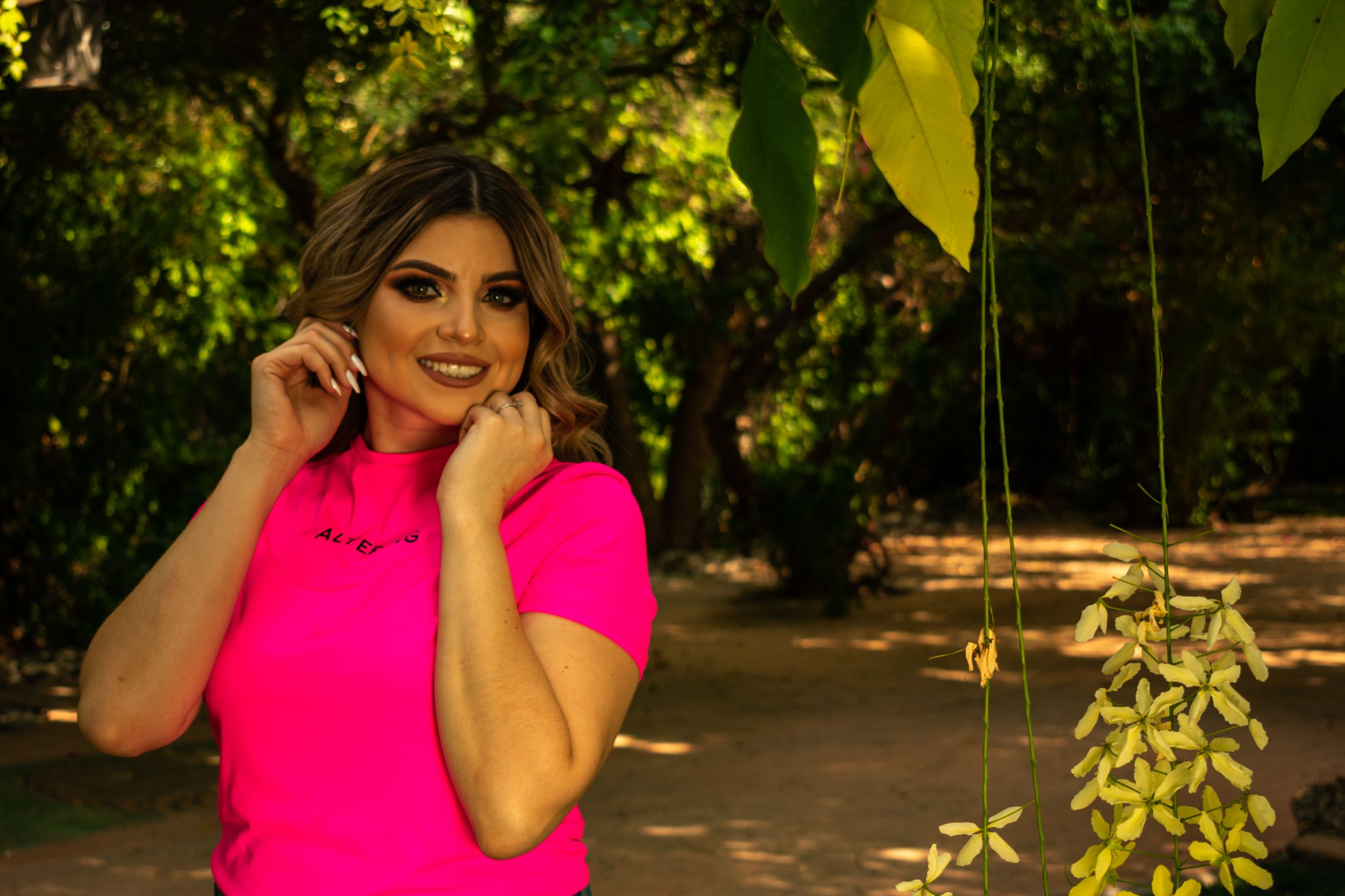 Fashion portrait in bright pink top against green garden backdrop.
