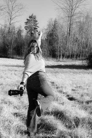 Black and white photo of photographer striking playful pose in outdoor field setting.